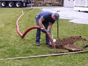 Septic pumping technician servicing a residential septic tank with a vacuum hose in Reading, MA