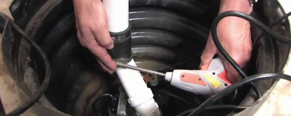 Sump pump installation technician connecting PVC discharge piping in Reading, MA