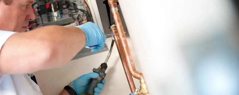 Water heater repair technician testing copper pipe connections and controls in Reading, MA